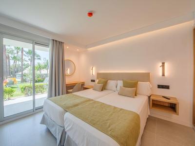 Modern eingerichtetes Hotelzimmer mit zwei Betten und Blick auf einen Garten durch Glas-Schiebetüren.