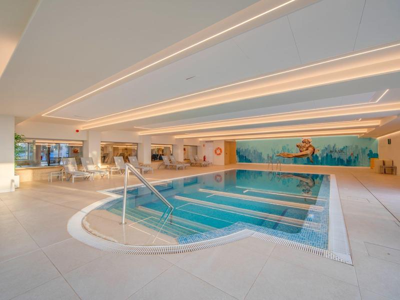 Modernes Hallenbad mit klaren Wasser, Mosaikwand und heller Beleuchtung.