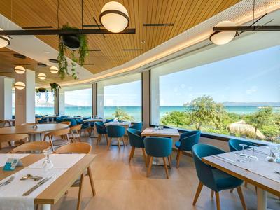 Moderner Speisesaal mit blauen Sesseln, Holztischen und großen Fenstern mit Meeresblick.