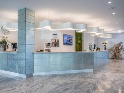 Moderner Empfangsbereich mit beleuchtetem Tresen, hellen Wänden, Marmorfußboden und Blumendekor.