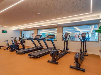 Moderner Fitnessraum mit Laufbändern und Crosstrainern, helle Beleuchtung und Fensterblick.