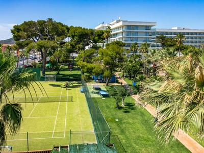 Hotelanlage mit Tennisplatz, umgeben von Palmen und viel Grün unter blauem Himmel.