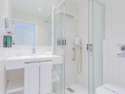 Helles, modernes Badezimmer mit Glasdusche, weißem Waschbecken und Handtüchern.