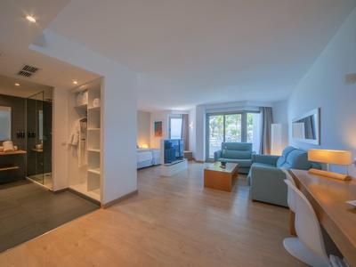 Helles, modernes Hotelzimmer mit Sitzbereich, Schreibtisch und offenem Badbereich.