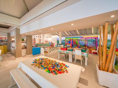 Heller und moderner Hotelspielbereich mit Tischen, Bausteinen und Kletterwand für Kinder.