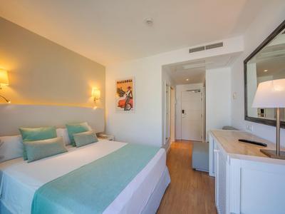 Modern eingerichtetes Hotelzimmer mit Doppelbett, blau-grüner Bettwäsche und hellem Holzfußboden.