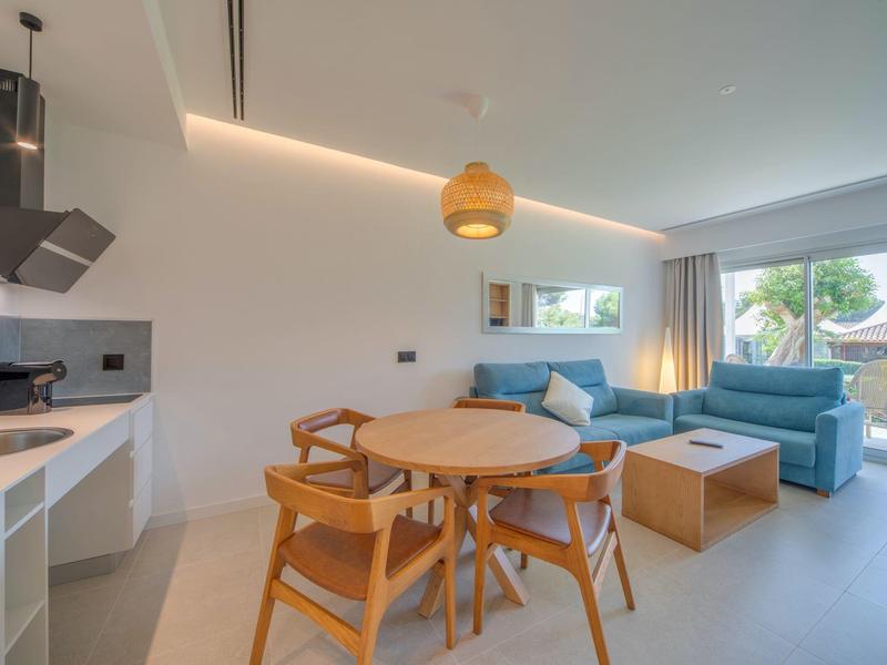 Helles Wohnzimmer mit Essbereich, Küchenzeile und Sofaecke mit großen Fenstern.