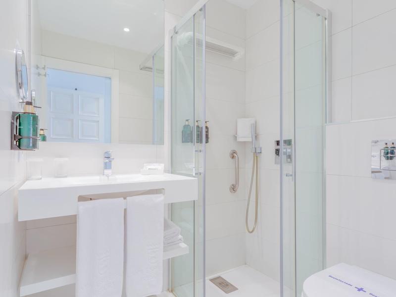 Helles, modernes Badezimmer mit Glasdusche, weißem Waschbecken und Handtüchern.