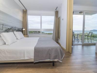Modern hotel room with double bed, large windows, and balcony with sea view.