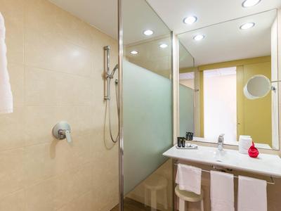 Modern hotel bathroom with shower, large mirror, and sink with towels.
