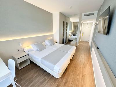 Modern hotel room with double bed, white furniture, and wooden floor.
