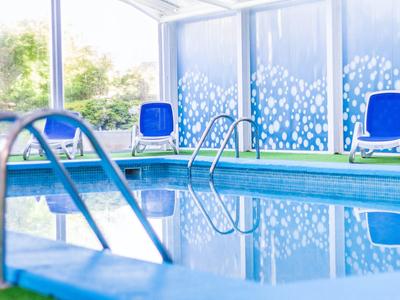 Piscina coperta con sedie a sdraio blu e grandi finestre che lasciano entrare la luce del giorno.