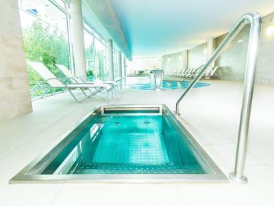 Piscina interna moderna con vasca idromassaggio, lettini e grande finestra con vista sul verde.