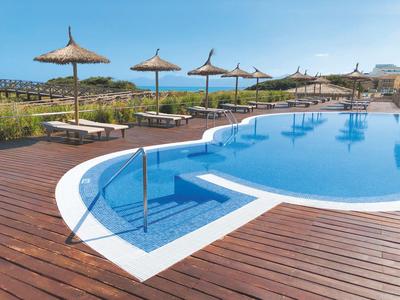 Leisure pool with wooden deck, sun loungers, and straw parasols overlooking the sea