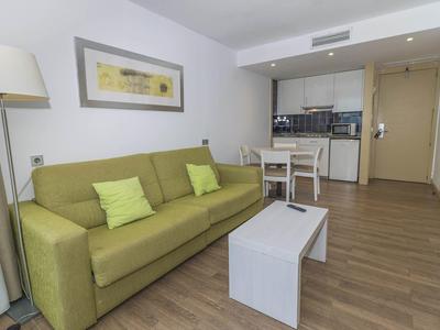 Salón de diseño moderno con sofá verde, mesa de centro blanca y cocina abierta.