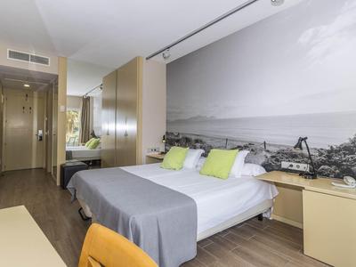 Habitación moderna con cama doble, lámparas, escritorio y mural costero en la pared.