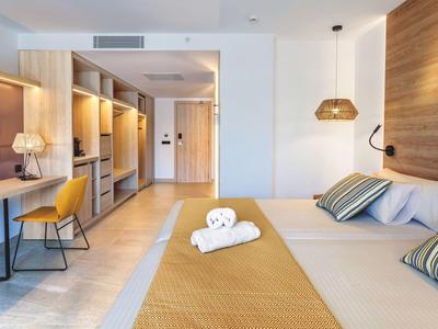 Chambre d'hôtel lumineuse avec lit double, bureau, armoires ouvertes et éclairage moderne.