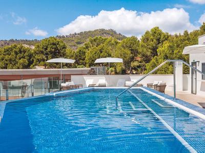 Modern outdoor pool with umbrellas and lounge chairs against wooded hills.
