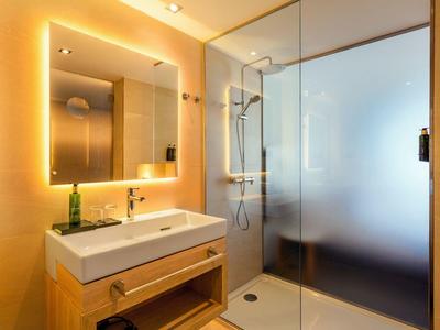 Bagno moderno con specchio illuminato, lavabo e ampia doccia in vetro.