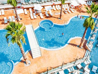 View of a tropical hotel pool with palm trees, lounge chairs, and umbrellas.