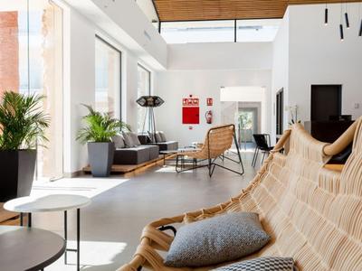 Moderner Wohnraum mit Holzdecke, weißen Wänden, großen Fenstern und Rattansesseln mit Kissen.