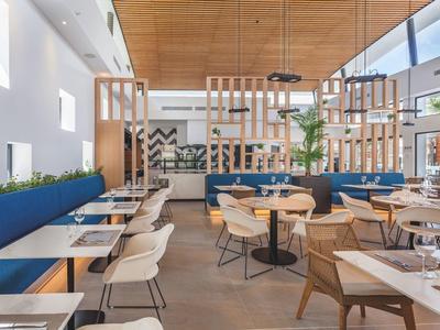 Modernes Restaurant mit blau gepolsterten Sitzbänken, Holztischen und hohen Decken mit Holzvertäfelung.