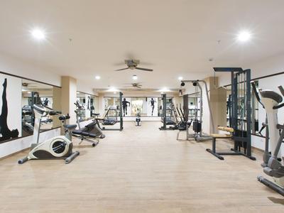 Nowoczesna siłownia z różnymi urządzeniami do ćwiczeń i dużymi lustrami na ścianach.