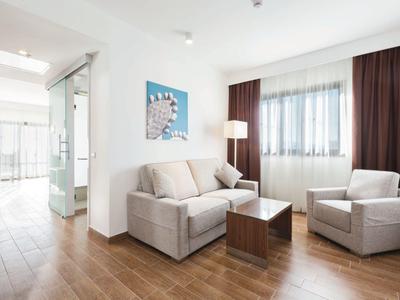 Mały salon z sofą, fotelem, stolikiem i naturalnym światłem w pokoju hotelowym.