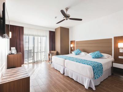 Modern hotel room with twin beds, wooden decor, ceiling fan, and balcony access.