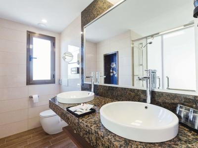 Modern hotel bathroom with double sinks, large mirror, window, and sleek fixtures.