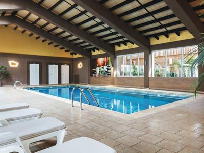 Indoor pool area with lounge chairs, large windows, and a high wooden ceiling.
