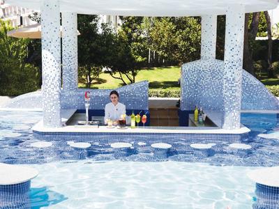 Outdoor pool bar with a bartender surrounded by mosaic tiles and clear blue water.