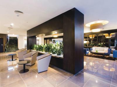 Lobby d'hôtel moderne avec fauteuils, tables et plantes décoratives.