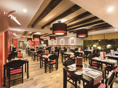 Salle de restaurant moderne avec tables noires, nappes blanches et poutres apparentes.