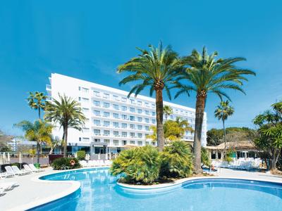 Hôtel moderne avec piscine extérieure entourée de palmiers sous un ciel bleu clair.