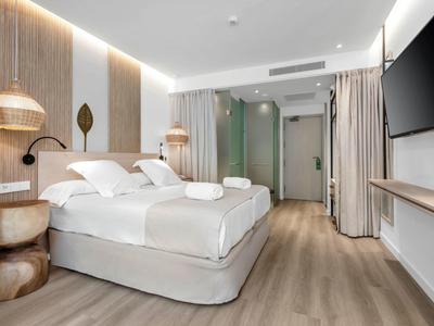 Nowoczesny pokój hotelowy z podwójnym łóżkiem, drewnianymi akcentami i dużym telewizorem.