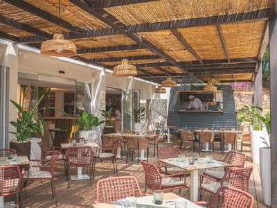 Überdachte Außenterrasse mit Tischen, Stühlen und einem großen Fernseher an der Wand