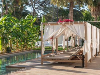 Bequeme Poolliegen mit weißen Vorhängen neben einem Pool in tropischer Umgebung.