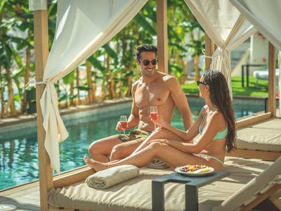 Una coppia si rilassa su una sdraio vicino alla piscina in un resort tropicale.