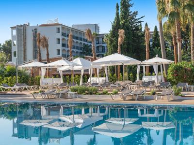 Hotelpool mit Liegestühlen und Sonnenschirmen vor einem mehrstöckigen Hotelgebäude.