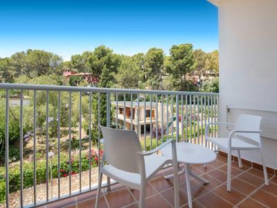 Balcony with white chairs and table overlooking trees and blue sky.