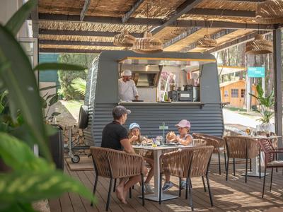 People sit outside in a shaded area in front of a small food truck.