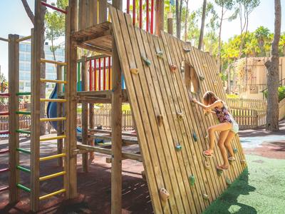 Child climbing a wooden playground wall with climbing holds in the sunshine.