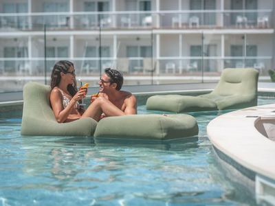 Due donne si rilassano su un galleggiante verde nella piscina accanto a un hotel moderno.