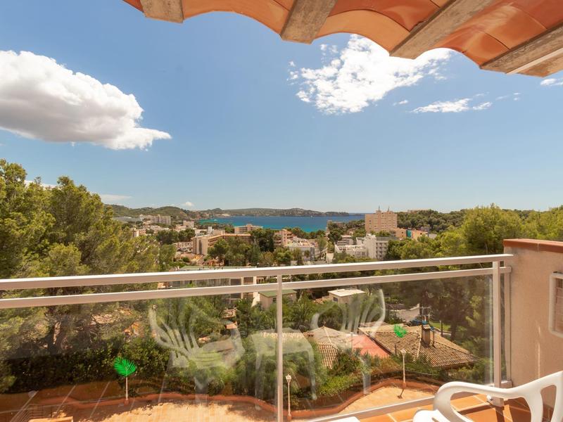 View from a terrace with glass railing over trees, buildings, and the sea in the background.