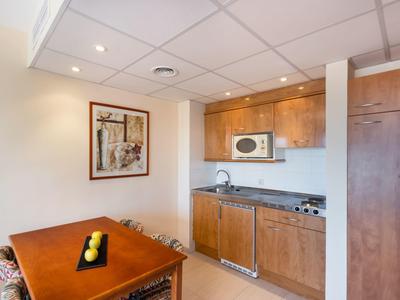 Petite kitchenette avec armoires en bois, micro-ondes et table à manger avec fruits.