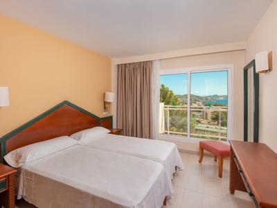 Chambre d'hôtel lumineuse avec deux lits, meubles en bois et balcon avec vue sur les montagnes.