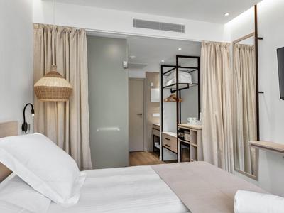 Chambre d'hôtel moderne avec lit, rideaux, télévision et penderie ouverte.