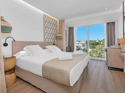 Chambre d'hôtel lumineuse avec lit double, balcon et vue sur des palmiers.