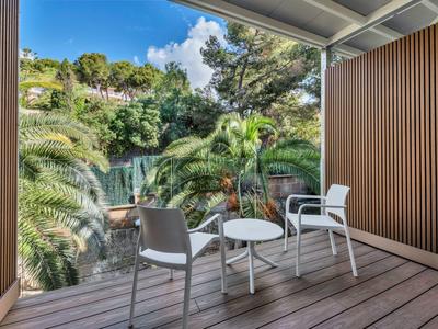 Balcon avec chaises blanches et table donnant sur des arbres tropicaux et un ciel bleu.